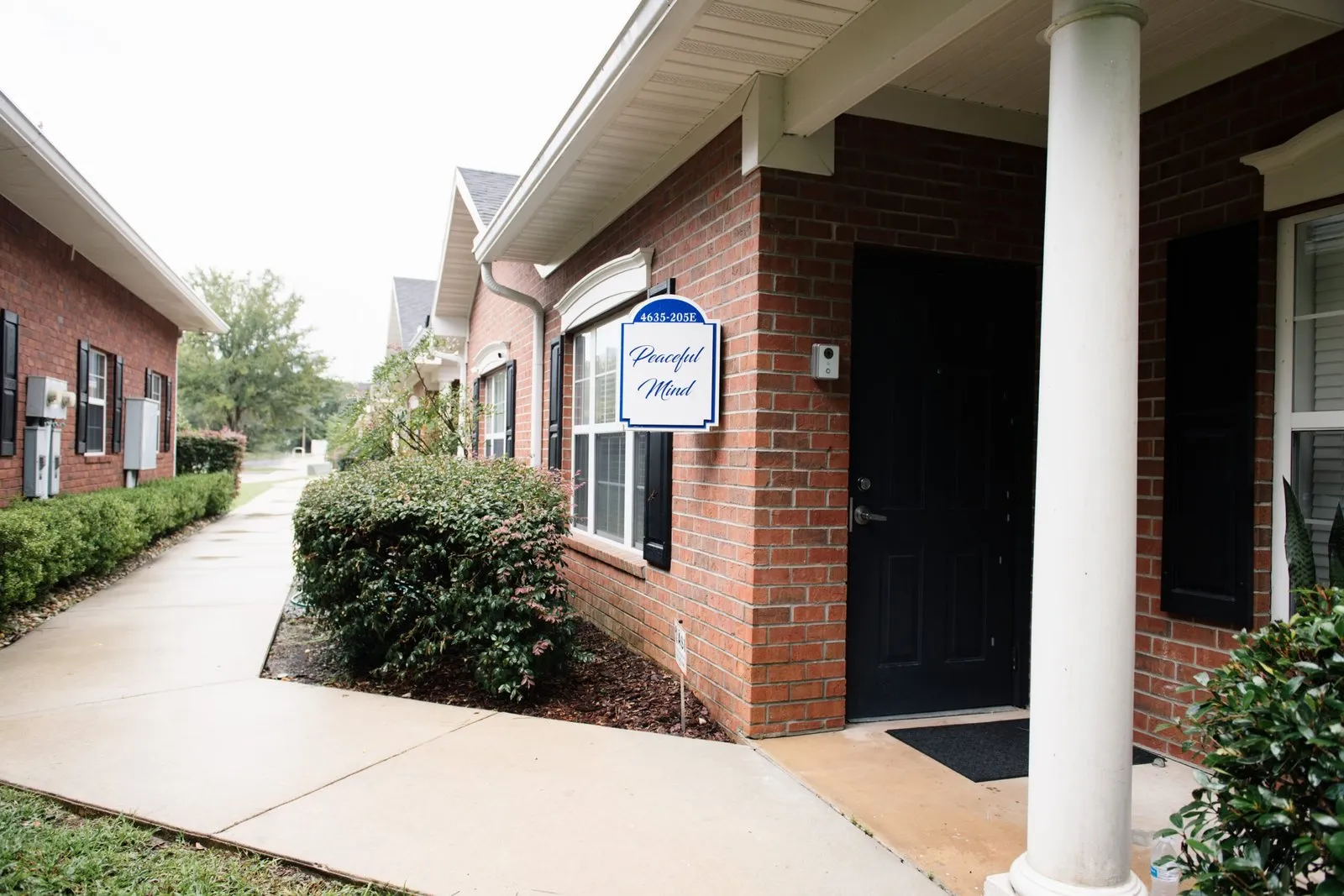 The suite entrance: a brick building with a white column, a dark door, and a small blue-and-white sign reading 4635-205E, Peaceful Mind.
