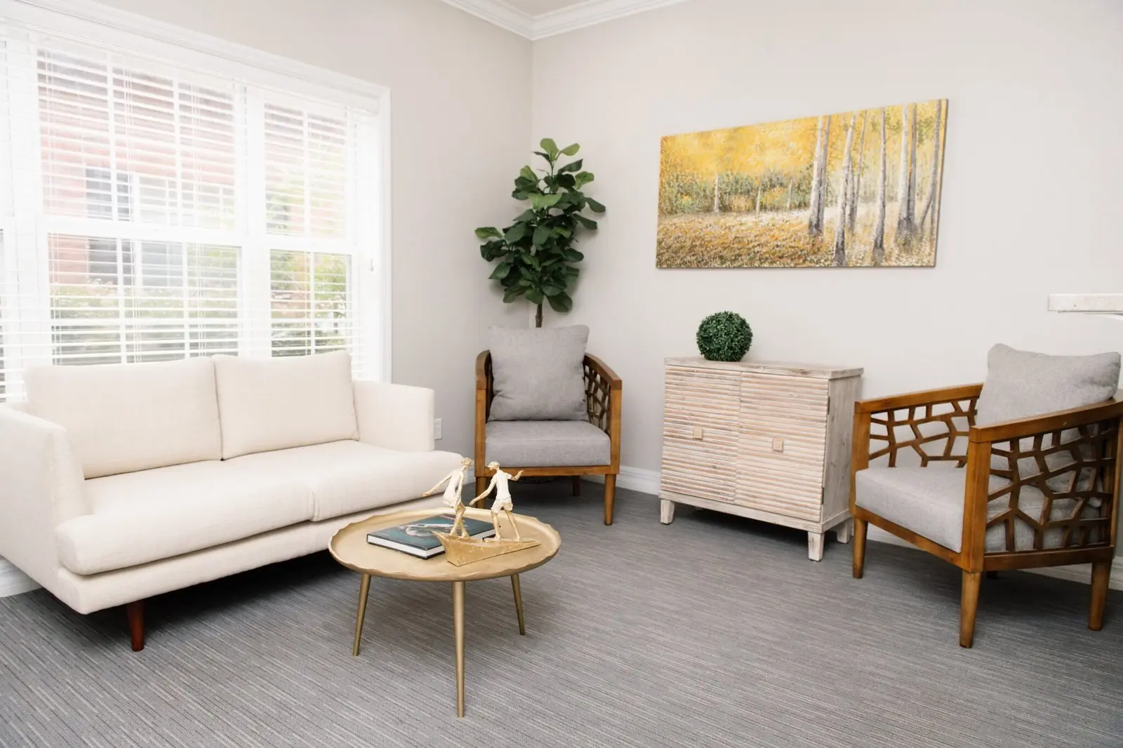 The practice waiting area: a pale sofa and two armchairs around a low table, beside a wide shuttered window, with a landscape painting on the wall.